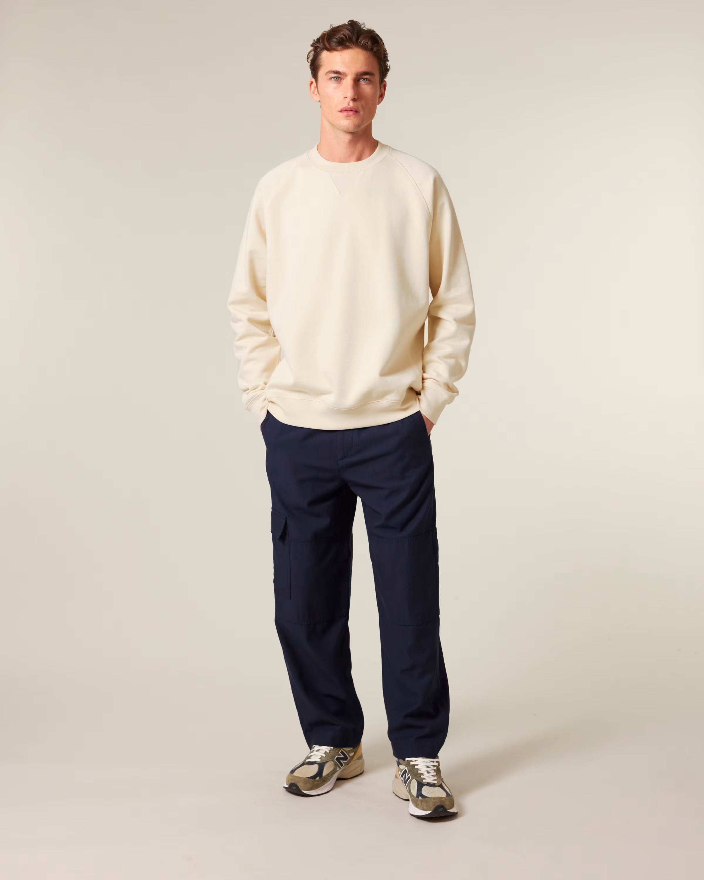Man wearing a cream sweater and navy pants against a plain background